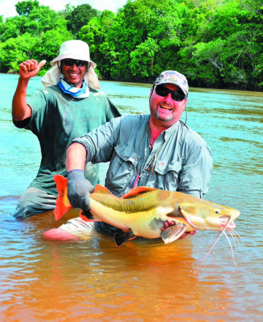 man in Amazon River with large red tail catfish
